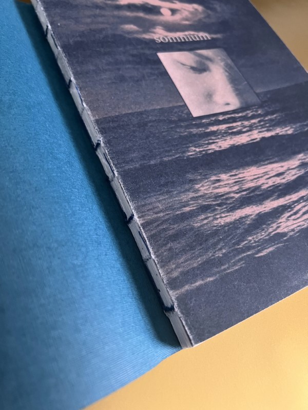 Close-up of the Somnium artist book's exposed Swiss binding, blue thread stitching